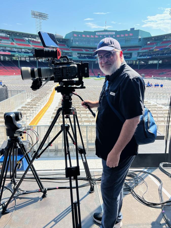 David McCauley beside a broadcast camera on a tripod at Fenway Park
